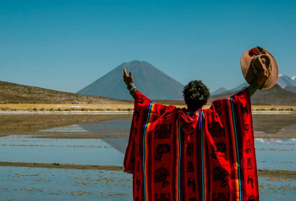 A person in colorful traditional attire raising a hat towards the majestic Misti Volcano in Arequipa, Peru.